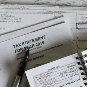A collection of tax documents and forms, including a tax statement for the year 2019, a pen, and an open notebook with handwritten notes.